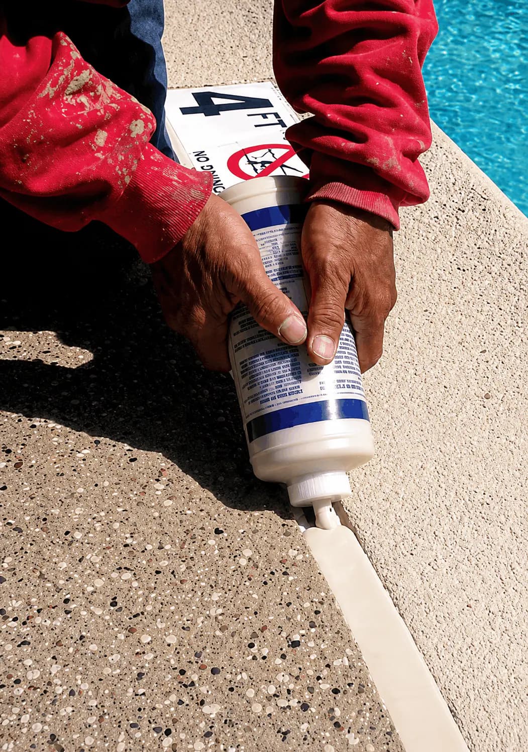 Pool professional applying new mastic seal around a residential swimming pool